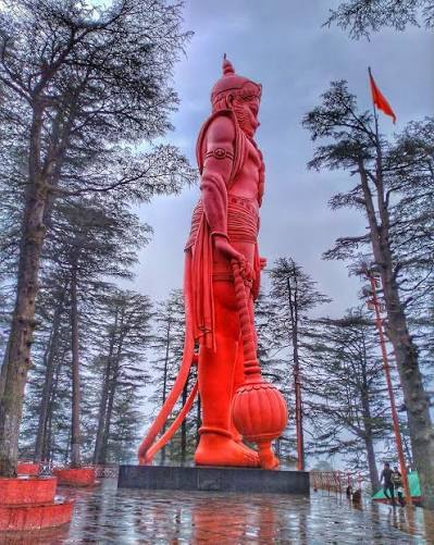 108 feet tall orange Lord Hanuman statue at Jakhoo Temple Shimla surrounded by pine trees
